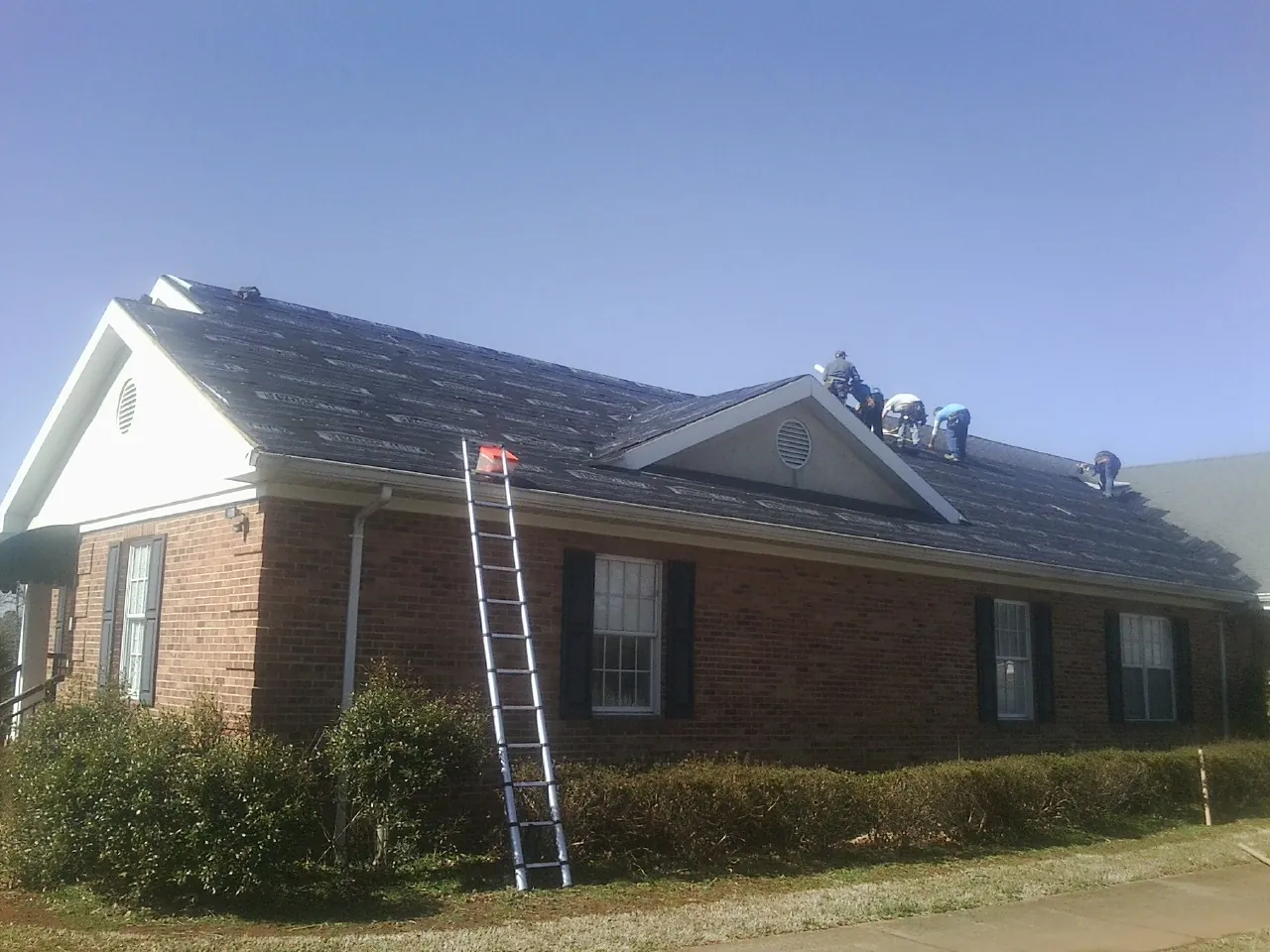 Crew tearing shingles off a brick ranch roof with a ladder set — Metal Roof Repair work by our crew in Huntingburg