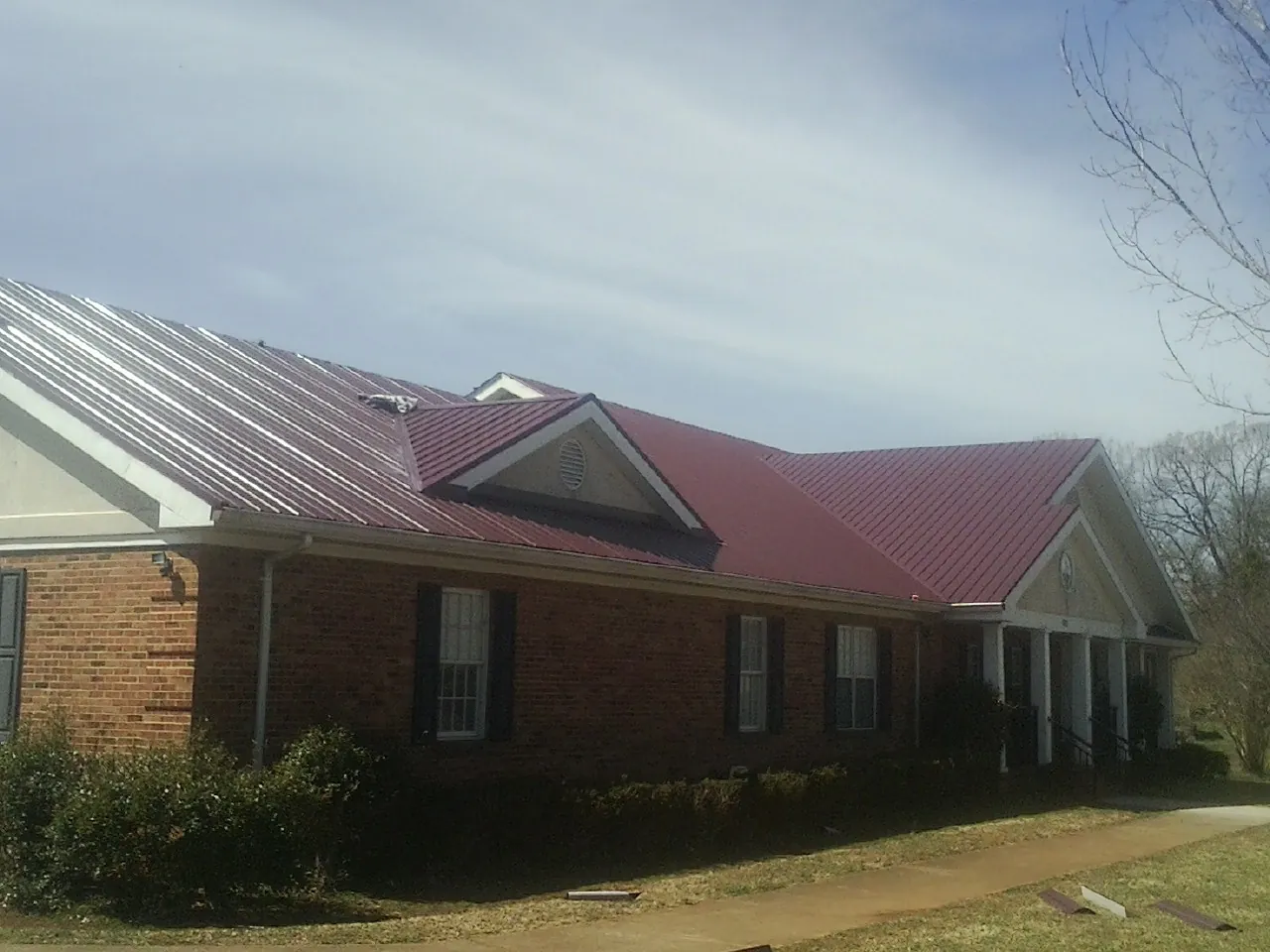 Red metal roof with gabled entries on a long brick building, from a Hail Damage Roof Repair job in Huntingburg