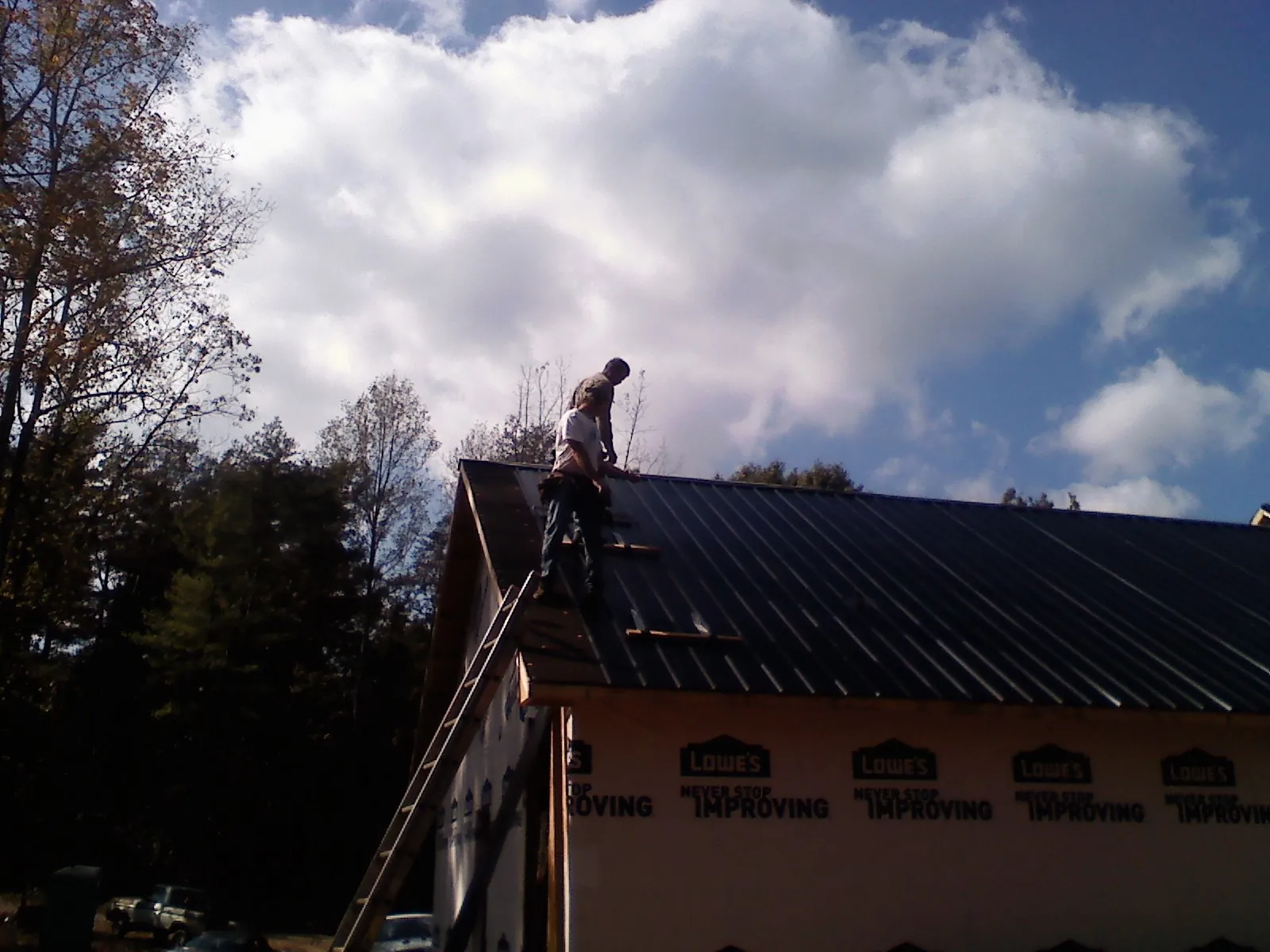 Roofer fastening dark metal panels high against a cloudy sky, from a Roof Inspection job in Huntingburg