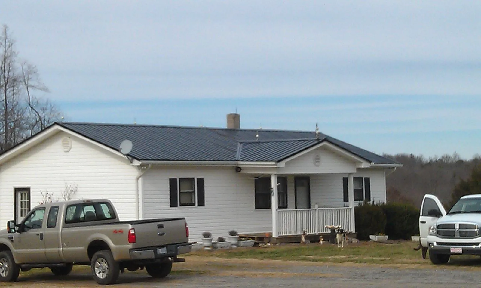 Finished dark metal roof on a white ranch home with work trucks parked in Huntingburg