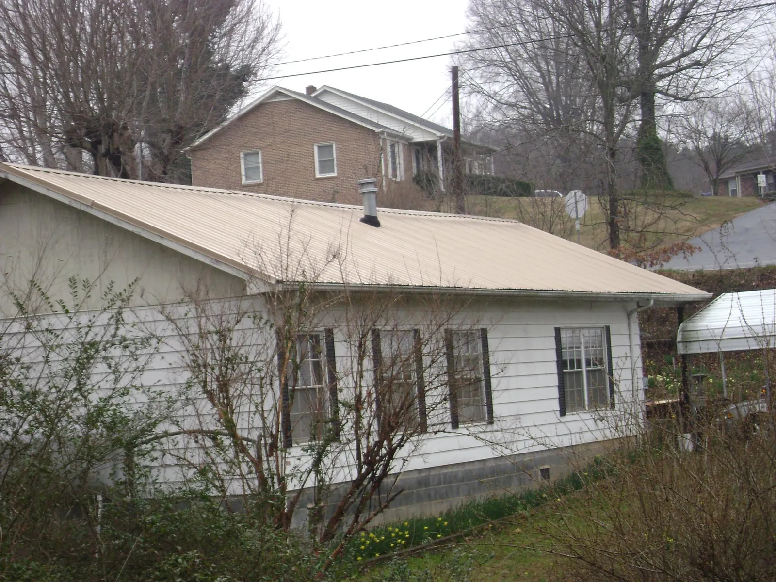 Tan metal roof on a white sided house set into a hillside — Commercial Roofing by Roofing Brothers in Huntingburg