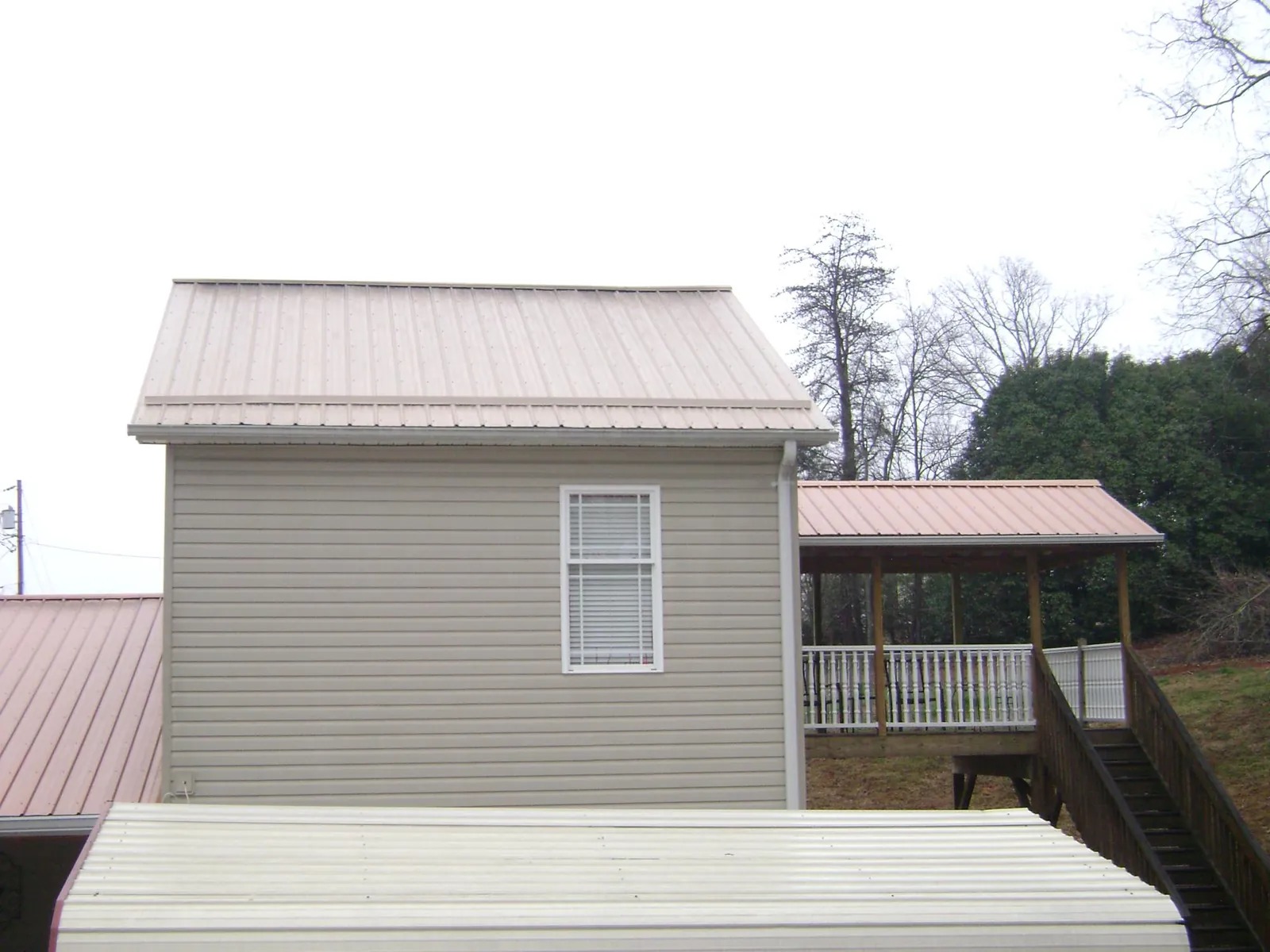 Tan metal roofs on a two story addition and attached porch, from a Roof Replacement job in Huntingburg